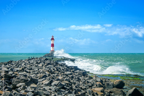 Large waves crash against the stone tower of the lighthouse at high tide