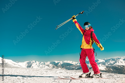 Happy young girl skier stands with ski poles at mountain top. Winter holidays concept