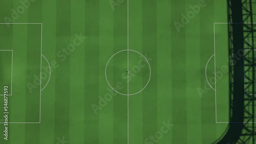 Camera zooms out from the middle of a full football or soccer stadium, soccer ball in the middle, top view. Kickoff moment.