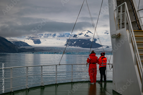 Two persons on the bow of a ship looking over the water at glacier and mountains photo