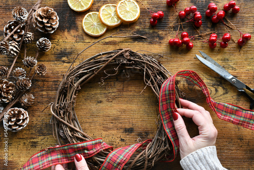 Female creating a winter holiday Christmas grapevine wreath with plaid ribbon, pine cones, dried lemons