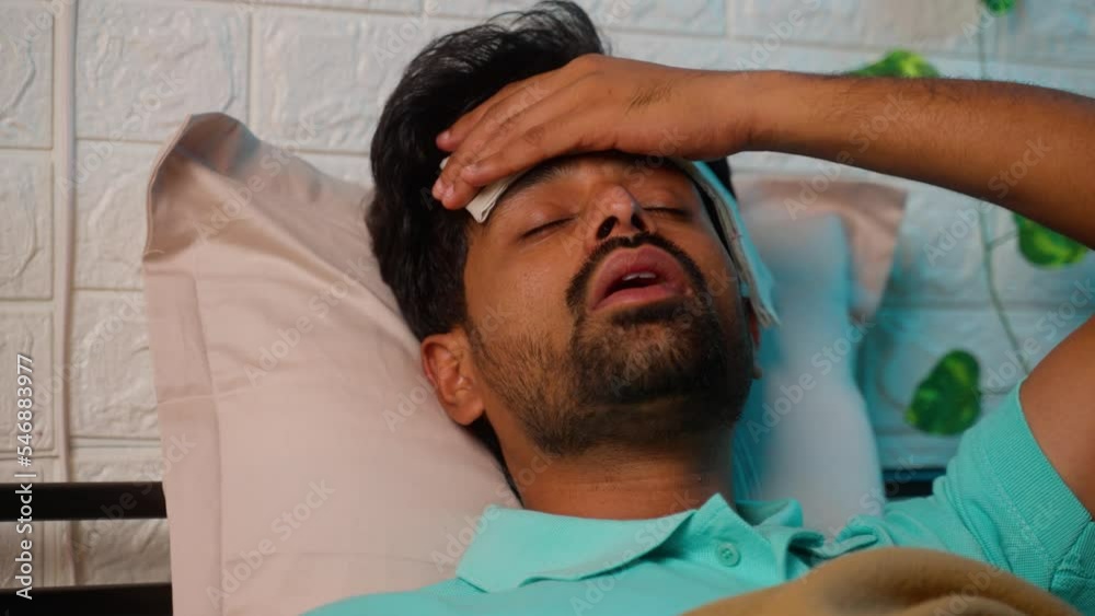 young indian sick man placing wet cloth on forehead to reduce