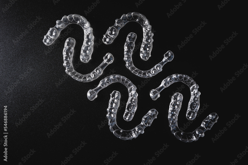 a pattern of invisible plastic aligners lie on a black background a pattern of invisible plastic aligners lie on a black background