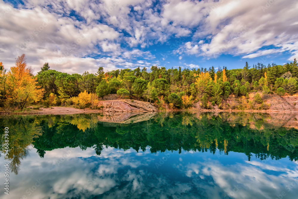 Scenic view of mirror like reflection of Carces lake in south of France in autumn colors against dramatic sky