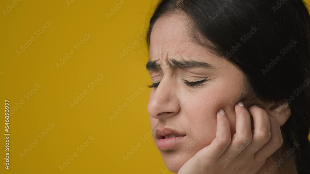 Close up portrait in studio yellow background Indian ethnic woman girl lady female suffer with toothache inflammation in gums dental damage infection touch cheek pain ache discomfort needs dentist Close up portrait in studio yellow background Indian ethnic woman girl lady female suffer with toothache inflammation in gums dental damage infection touch cheek pain ache discomfort needs dentist