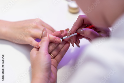 Close-up of a girl doing a manicure in a beauty salon. Nail care. Manicurist paints the corners on the nails with a brush with white varnish. Cosmetic procedure