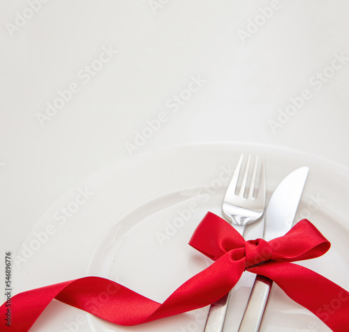 Holiday table setting close up. Cutlery and red satin ribbon decoration on white dishes,