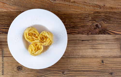 Raw pasta in white plate on wooden background, top view, copy space