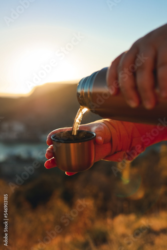 A human pours hot tea from a thermos into a mug on the mountain. Concept of autumn outdoor recreation. 