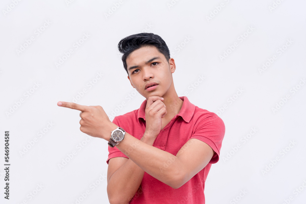 A bewildered young man points to something on the left while getting second thoughts. Looking at the camera with wide eyes and thinking. Isolated on a white background. A bewildered young man points to something on the left while getting second thoughts. Looking at the camera with wide eyes and thinking. Isolated on a white background.