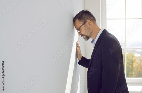 Man gets bankrupt, loses business, feels overworked defeated frustrated unsuccessful hopeless disappointed tired of stress, finance economy problems, debts, bangs head against light gray office wall