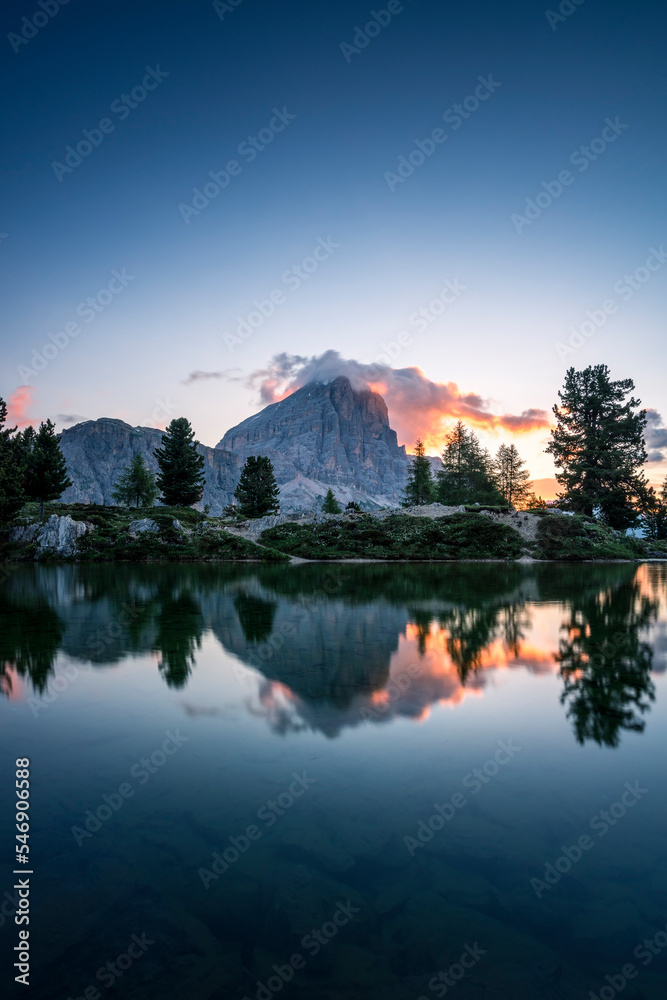 Bergsee mit Spiegelung zum Sonnenaufgang mit leuchtenden Wolken in den Dolomiten.