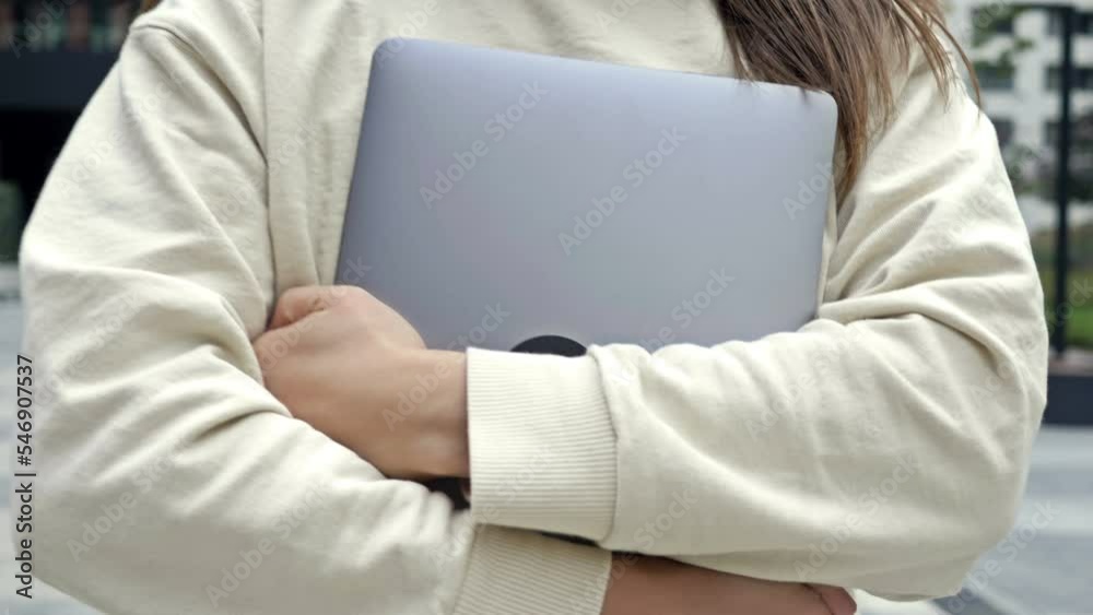 Woman with a laptop in her hands walks along the street of a large modern city. Woman with a laptop in her hands walks along the street of a large modern city.