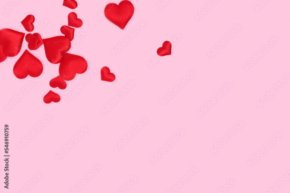 Red textile hearts confetti scattered on a pink pastel background.