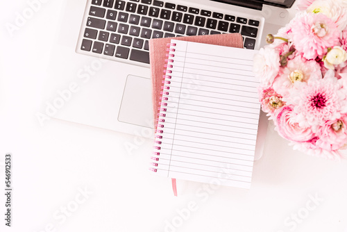 A femininely styled desktop in shades in gold and dusty pink with modem stationery. Lifestyle theme inspired by the office workspace of a stylish woman. Flat lay with fresh flowers pink keyboard and photo