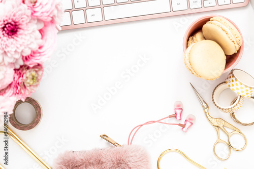 A femininely styled desktop in shades in gold and dusty pink with modem stationery. Lifestyle theme inspired by the office workspace of a stylish woman. Flat lay with fresh flowers pink keyboard and photo