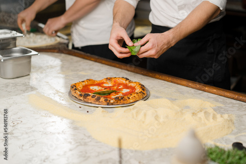 Professional chef decorating Margherita pizza in restaurant kitchen. Traditional italian cuisine