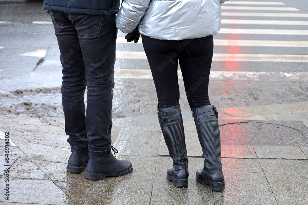Couple on pedestrian crossing holding hands. Road zebra marking, people on wet crosswalk in snow weather, street safety concept