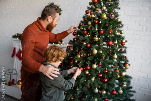 redhead kid with bearded father decorating Christmas tree in living room at home