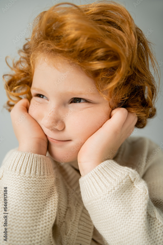 Portrait of red haired kid in beige knitted jumper looking away isolated on grey Portrait of red haired kid in beige knitted jumper looking away isolated on grey