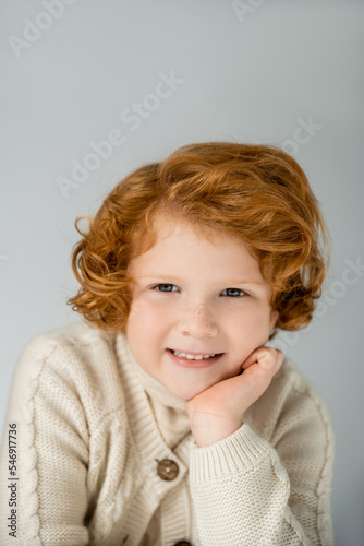 Portrait of smiling redhead boy in knitted jumper looking at camera isolated on grey
