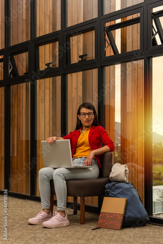 Young Latin woman sitting indoors with her laptop on her legs resting her hand on the screen with a defiant expression