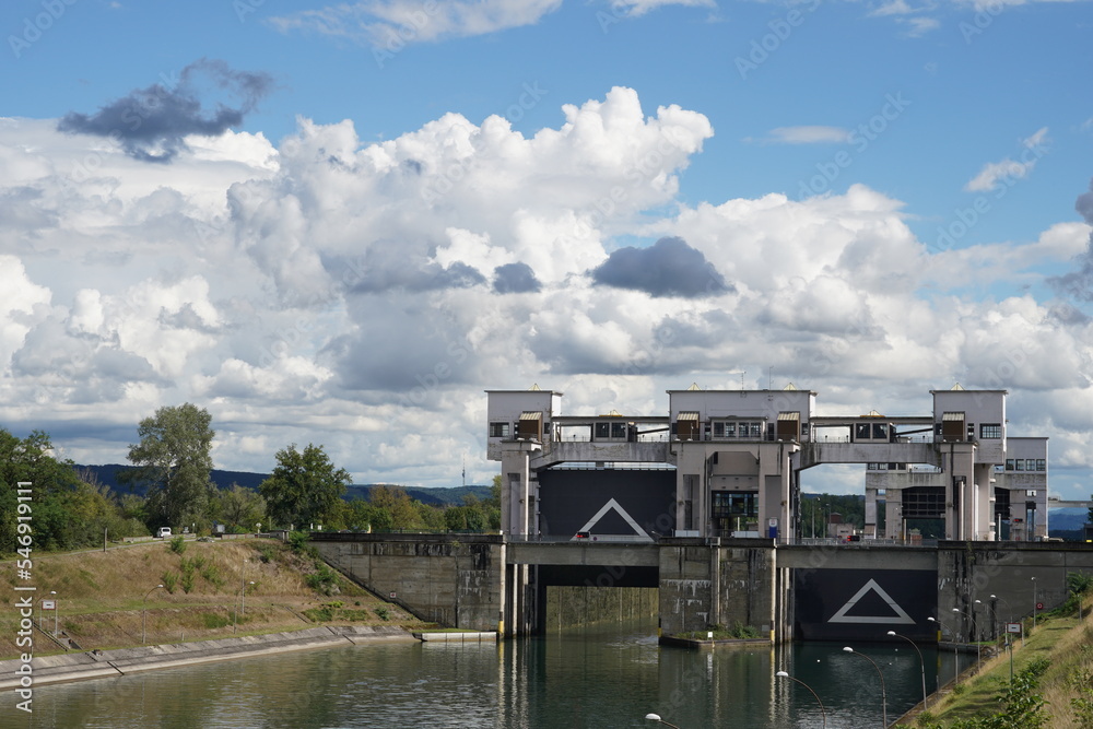 View on two locks with open one gate situated next to hydroelectric power station Kembs on the river Rhine. On the both doors are white triangles. On sides are grass banks. View on two locks with open one gate situated next to hydroelectric power station Kembs on the river Rhine. On the both doors are white triangles. On sides are grass banks.