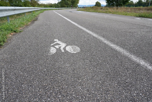 Bike lane or cycle path along the car road in the vicinity of hydroelectric power plant Kembs in France. The biking symbols and the line are painted in white color. In forward are visible cyclists.