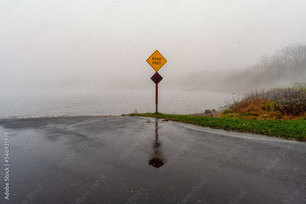Road Ends sign in front of a lake on a foggy misty day