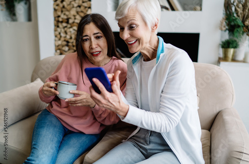 Cheerful multiethnic women with drink and cellphone having fun together