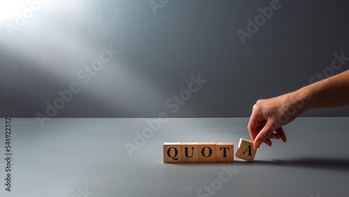 womans hand posing wooden block with the word quota . cocept of work Quota's .equality. photo
