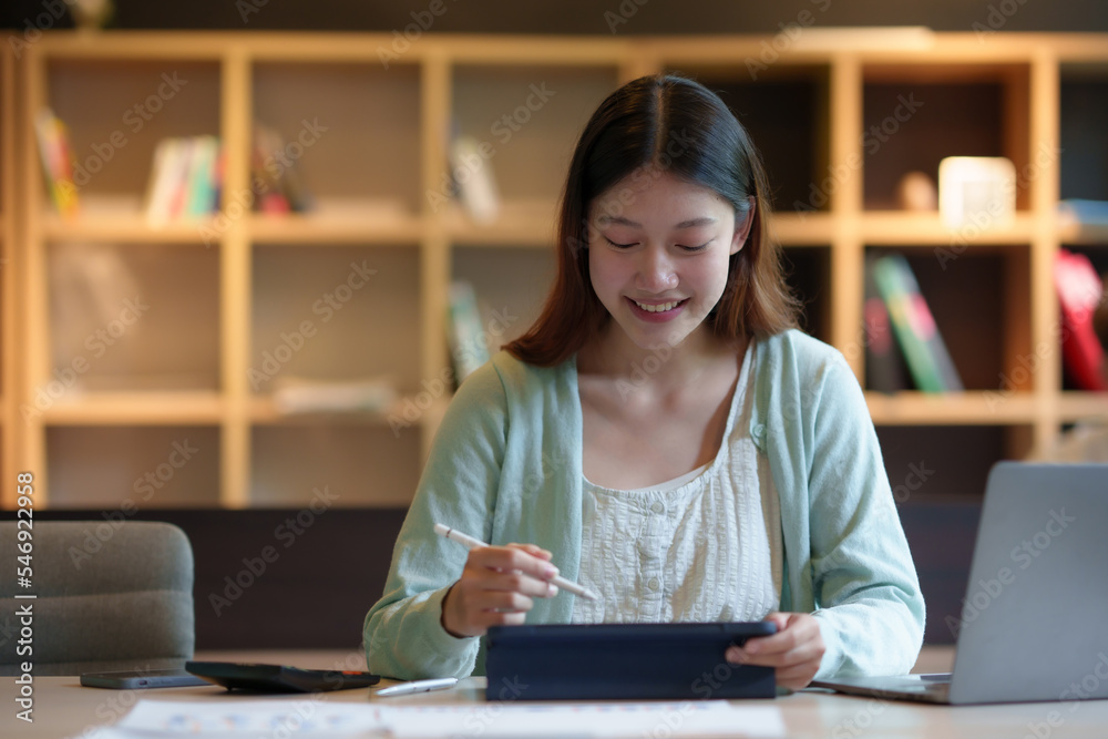 Beautiful, smiling young Asian woman student using a tablet to study online at home in the comfort of her own home. Beautiful, smiling young Asian woman student using a tablet to study online at home in the comfort of her own home.