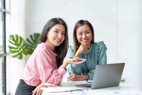 Two Asian businesswoman talk, discuss, work together to exchange ideas, presenting new start-up project ideas analyze marketing plans and office investments. © amnaj