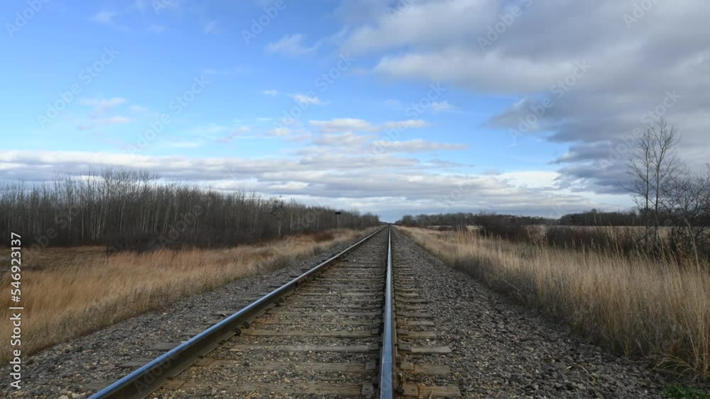 Time lapse looking down a railroad track with dry grass moving quickly in the wind and clouds moving in a blue sky.
Time lapse looking down a railroad track with dry grass moving quickly in the wind and clouds moving in a blue sky.