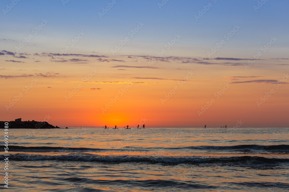 Beautiful sunrise on the beach with reflections of the sun in the sea with silhouettes of people on paddle boards