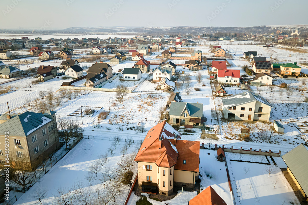 Fototapeta premium Aerial view of residential houses with snow covered roofops in suburban rural town area in winter