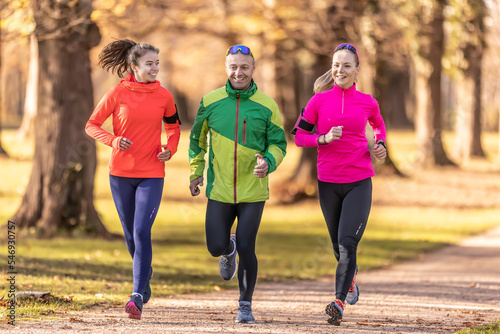 A trio of runners, two young women and one mature man are running in an autumn park