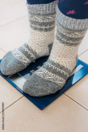 A woman in gray warm socks stands on the scales, weighs herself after gluttony during the holidays
