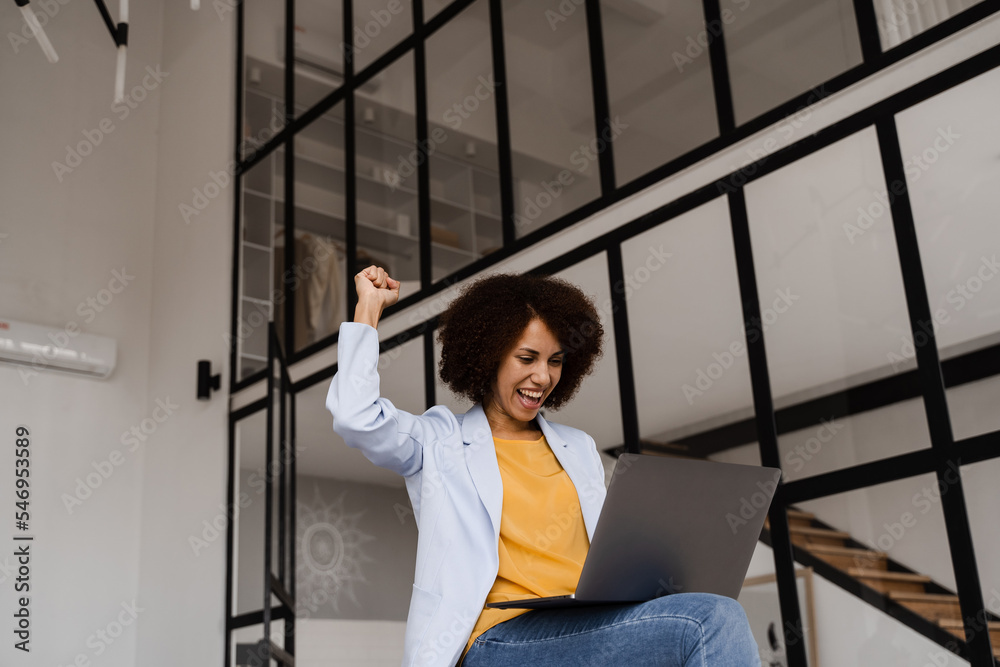 Happy afircan girl with laptop rejoices in winning bet in online casino. Cheerful surprised woman smile and looking at amount of income earnings salary and rejoices.