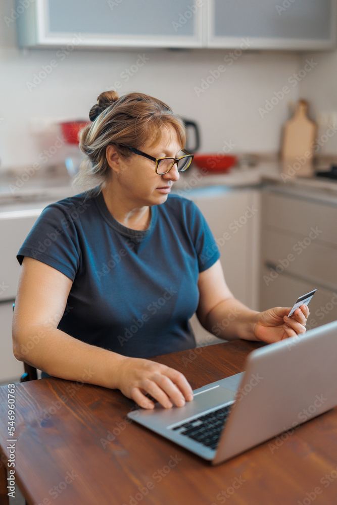 Mature woman using credit card making online payment at home. Successful old woman doing online shopping using laptop. Closeup of retired lady holding debit card for internet banking Mature woman using credit card making online payment at home. Successful old woman doing online shopping using laptop. Closeup of retired lady holding debit card for internet banking