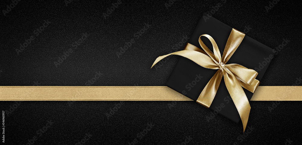 Obraz premium Blank gift greeting card with gift box present and bright shiny golden ribbon bow tape isolated on black background, top view and copy space for merry Christmas template or shopping advertising banner