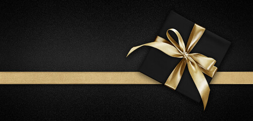 Blank gift greeting card with gift box present and bright shiny golden ribbon bow tape isolated on black background, top view and copy space for merry Christmas template or shopping advertising banner