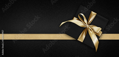 Blank gift greeting card with gift box present and bright shiny golden ribbon bow tape isolated on black background, top view and copy space for merry Christmas template or shopping advertising banner