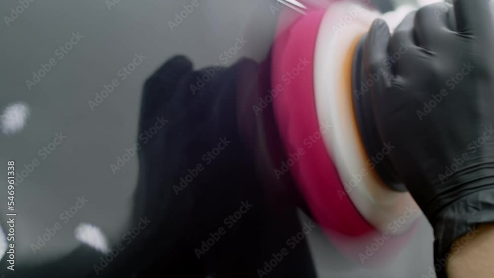 Hand of auto technician polishing car detail with sander. Close-up view. A man in a black glove polishes the surface of a black car with a polishing machine. Hand of auto technician polishing car detail with sander. Close-up view. A man in a black glove polishes the surface of a black car with a polishing machine.