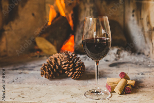 Taça de vinho tinto em lareira no inverno com rolhas e pinhas photo