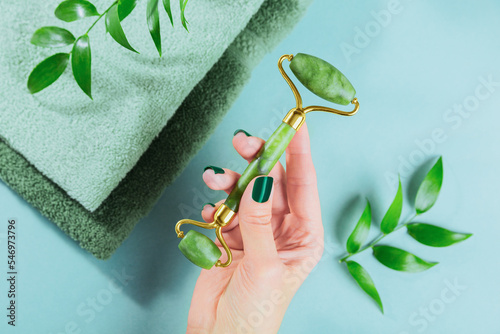 Fotobehang Female hand holding massage roller for the face with two heads of green jade stone
