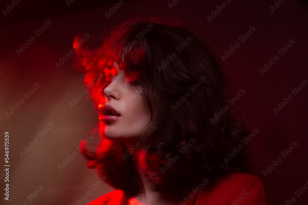 Closeup view of young woman with makeup and hairstyle, wear red suit, with closed eyes, red studio light and effects. Closeup view of young woman with makeup and hairstyle, wear red suit, with closed eyes, red studio light and effects.