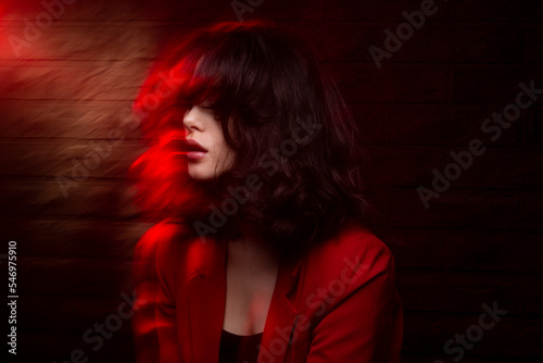 Fashion image of young woman with makeup and hairstyle, wear red suit, with closed eyes, red neon studio light.
