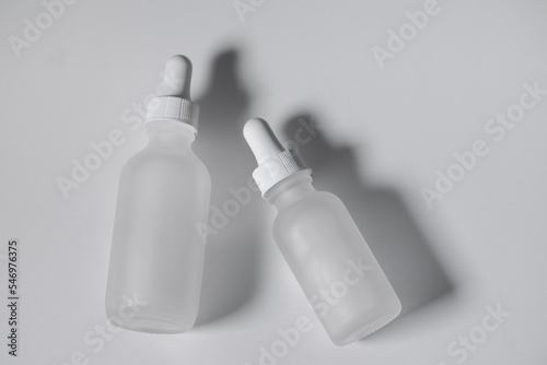 Close-up of two empty white translucent glass dropper vials, both bottles closed. Flatlay on white surface. Horizontal beauty and lifestyle background, mockup, and copy space. Professional lighting.