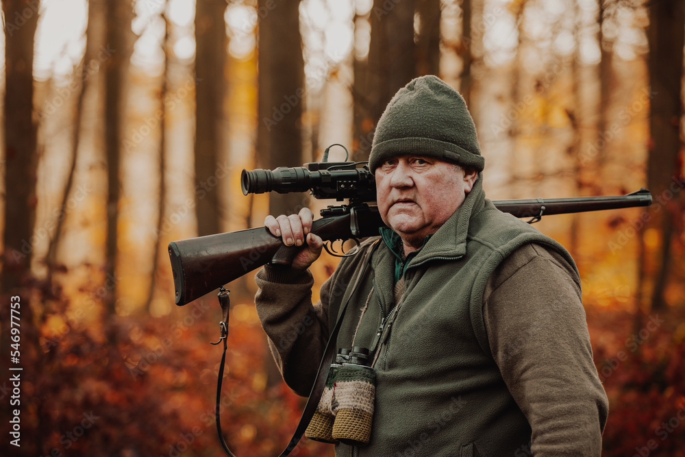 Portrait of hunter or ranger with gun or rifle in the forest looking out or hunting of some venison, hunting period, autumn season, hunting and people concept